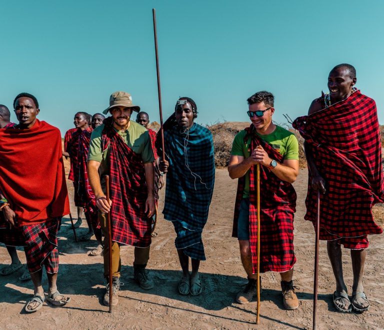 Maasai landowners and a safari guide standing together at sunrise on open grassland in a Kenyan wildlife conservancy