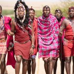 Maasai landowners and a conservancy ranger meeting near a grazing boundary marker at dawn, open grassland conservancy