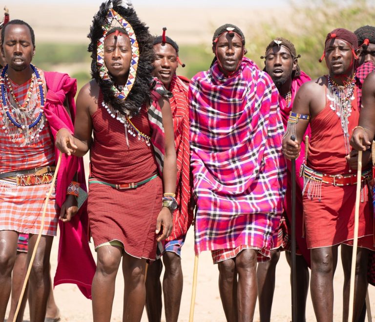 Maasai landowners and a conservancy ranger meeting near a grazing boundary marker at dawn, open grassland conservancy
