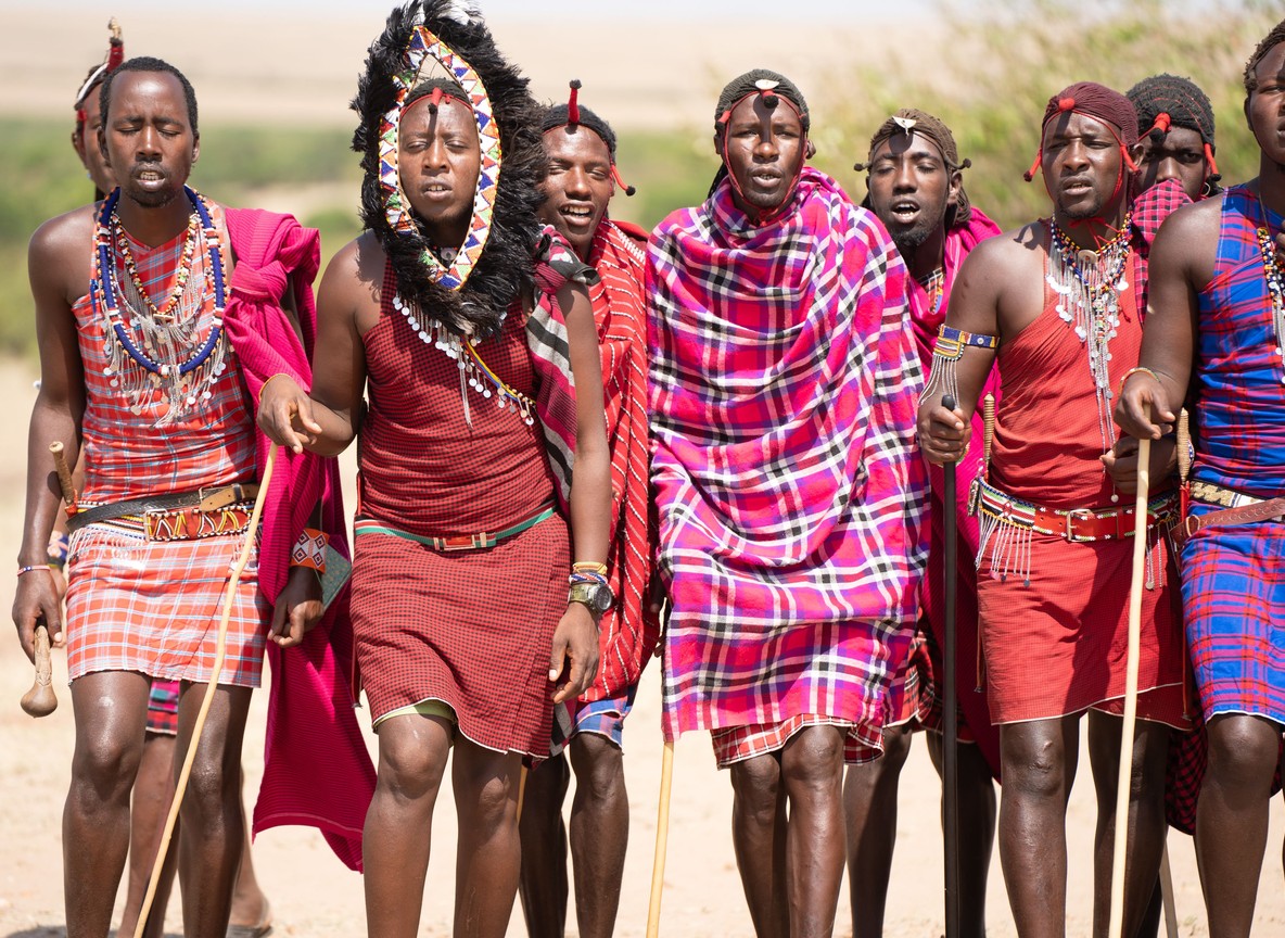 Maasai landowners and a conservancy ranger meeting near a grazing boundary marker at dawn, open grassland conservancy
