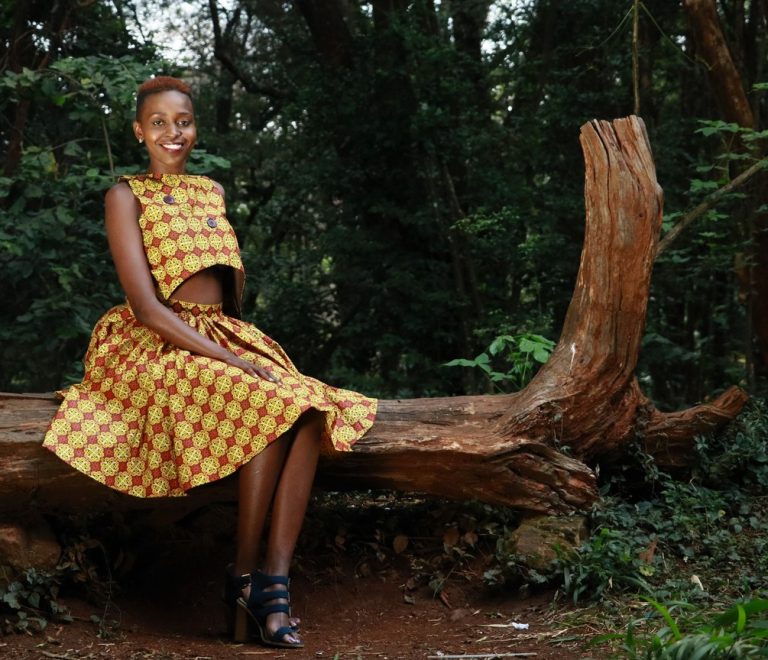 a solo woman traveler smiling and checking her phone in a bright, quiet Nairobi hotel courtyard with luggage beside her