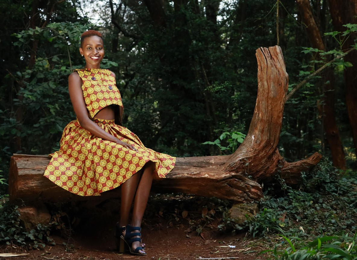 a solo woman traveler smiling and checking her phone in a bright, quiet Nairobi hotel courtyard with luggage beside her