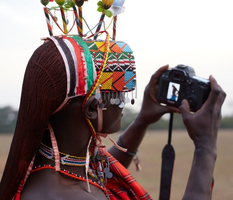 Pokot elder in traditional beaded ornaments standing in the West Pokot hills at golden hour, respectful documentary portrait