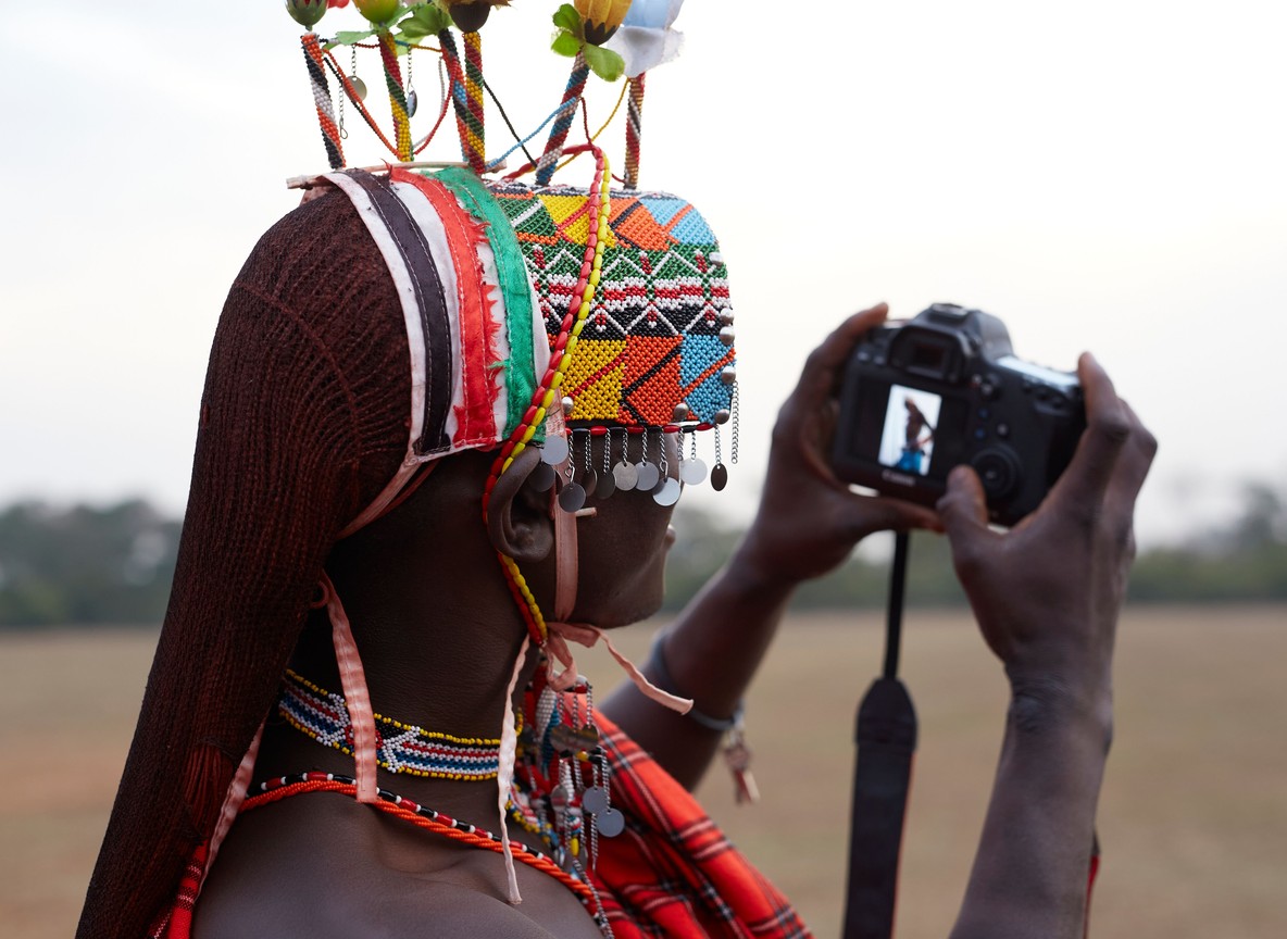 Pokot elder in traditional beaded ornaments standing in the West Pokot hills at golden hour, respectful documentary portrait